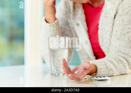 Donna che mantiene pillole con un bicchiere di acqua Foto Stock