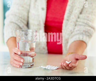 Donna che mantiene pillole con un bicchiere di acqua Foto Stock