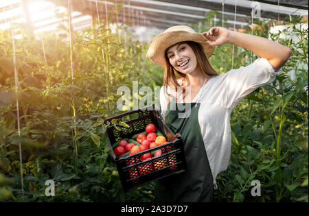 Ritratto di giovane agricoltore ragazza nel cappello di paglia in posa con una cassa di ortaggi Foto Stock