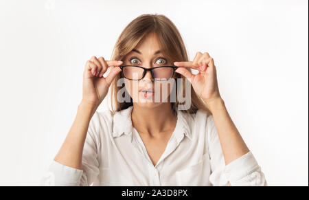Stupiti Donna che guarda la telecamera sopra gli occhiali, sfondo bianco Foto Stock