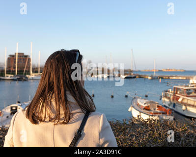 Schicke Frau schaut in einen Hafen mit Booten während eines Sonnenuntergangs Foto Stock