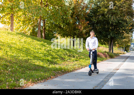 Gioioso e uomo informale equitazione scooter elettrico nel parco della città Foto Stock