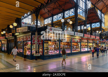 Un macellaio con appesi salumi e insaccati nel grande mercato coperto di Budapest, Ungheria Foto Stock