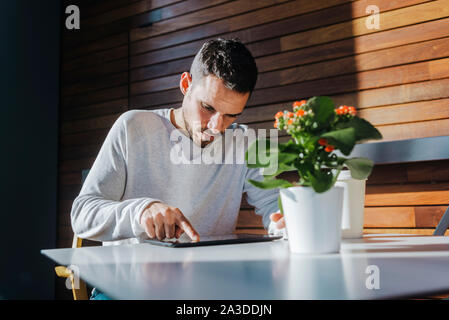 Elegante giovane uomo seduto sul lettino in un cafe utilizzando tablet Foto Stock