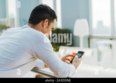Giovane uomo appoggiato sulla ringhiera mentre si utilizza il telefono cellulare Foto Stock