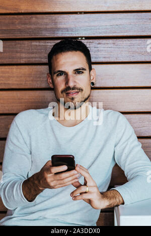 Giovane uomo in ufficio scuro tenendo lo smartphone e guardando la fotocamera Foto Stock