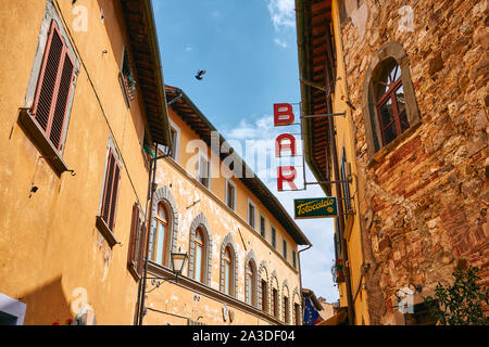 Basso angolo di barra rossa cartello sul lato dell antico edificio sulla strada stretta sotto il cielo blu in Toscana Foto Stock