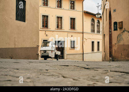 Vecchio triciclo bianco parcheggiato sulla strada collinare tra squallide case in Toscana Italia Foto Stock