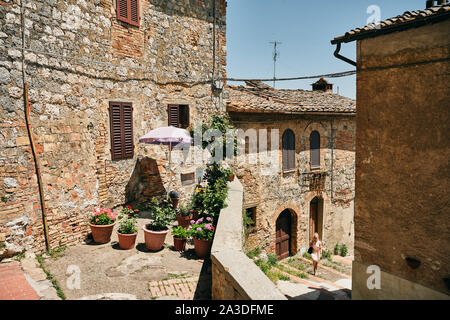 Pentole con rigogliosi houseplants posto sul balcone a spiovente di età compresa tra i mattoni casa sulla strada di città vecchia sulla giornata di sole in Toscana, Italia Foto Stock