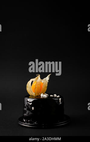 Organic Deep Dark Chocolate torta decorata con physalis su sfondo nero. Spazio di copia, verticale, vista frontale Foto Stock