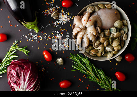 Materie di vongole fresche con il polpo, pomodori ciliegia, melanzana, cavolo rosso,sale pepe e rosmarino su sfondo nero. Concetto di frutti di mare Foto Stock