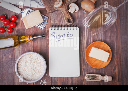 Ingredienti per fare il risotto disposti in un telaio e blocco di carta al centro su sfondo di legno Foto Stock