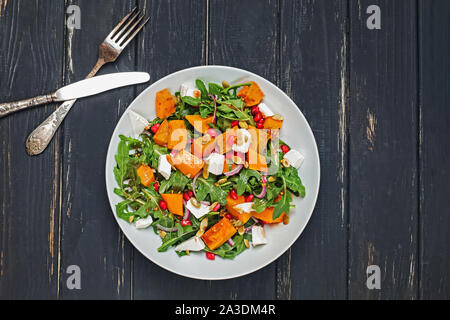 Insalata con la zucca, rucola, il formaggio feta e i semi di melograno su tavoli in legno nero Foto Stock