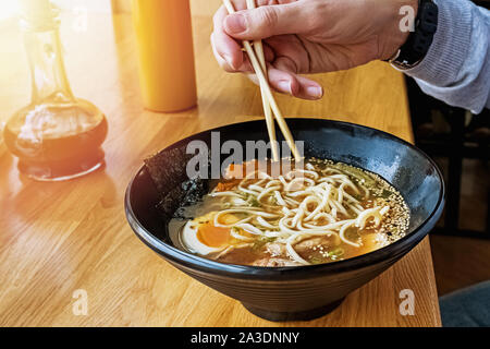 L'uomo le mani vicino le bacchette di contenimento vicino alla ciotola con deliziosi ramen caldo. Foto Stock