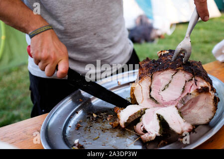 Uomo taglio in fette una deliziosa porchetta, italiano tradizionale cibo di strada Foto Stock