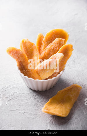 Disidratato ed essiccato mango chip nella ciotola bianco su calcestruzzo sfondo luminoso. Close up. Foto Stock