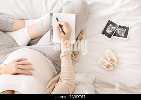 Donna incinta la preparazione per la manodopera per seduta sul letto con i notebook Foto Stock