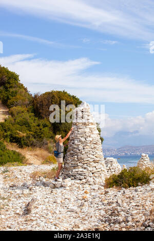Donna posizionando la posa di una pietra di ghiaia su un tumulo sulla spiaggia vicino il greco holiday resort di Kassiopi Corfù Grecia Foto Stock