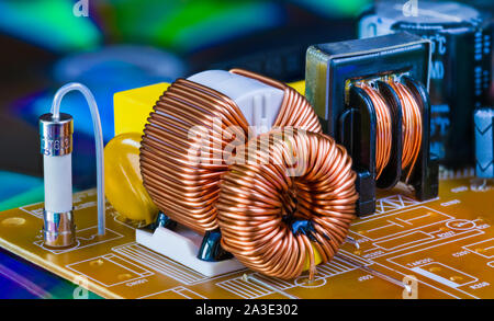 Induttori toroidali con avvolgimento in filo di rame, trasformatore e fusibile elettrico. I componenti elettronici sulla scheda a circuito stampato. Smontaggio della scatola di alimentazione particolare. Foto Stock