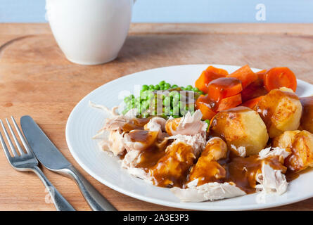 Un pollo arrosto cena su una piastra bianca con posate e una salsiera in background Foto Stock