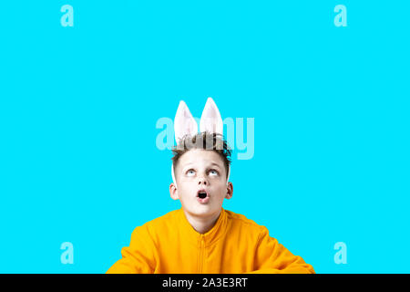 Ragazzo sorpreso in una giacca gialla e le orecchie di lepre su uno sfondo blu Foto Stock