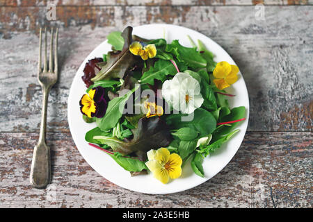 Bel mix di insalate con fiori su una piastra bianca. Concetto di dieta. Nutrizione per le ragazze. Sano cibo vegan. Foto Stock