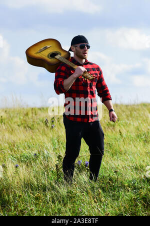 Uniti con la natura. La vacanza estiva. Trasognata wanderer. Atmosfera pacifica. Escursionismo canzone. Un musicista in cerca di ispirazione. Ispirando la natura. Uomo bello con la chitarra a contemplare la natura. In cerca di muse. Foto Stock