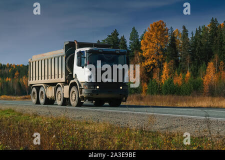 Un carrello che trasporta merci lungo una strada forestale contro lo sfondo di una foresta di autunno e cielo blu . Foto Stock