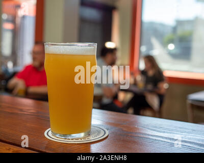 Completa di vetro pinta di birra IPA seduti su un tavolo di legno alla birreria ristorante con persone di background Foto Stock