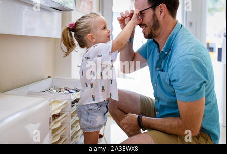 La cura della salute, la vista e il concetto di visione. Bambina scelta di occhiali con padre al negozio di ottica Foto Stock