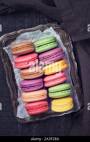 Macaron colorati al buio su un sfondo di legno Foto Stock