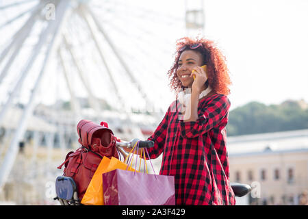 Curly giovane donna che chiama il suo amico dopo lo shopping Foto Stock