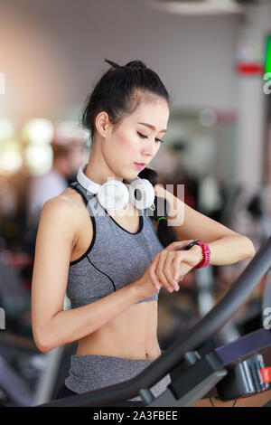 Centro fitness donna che indossa le cuffie utilizzare lo sport watch per cardio allenamento in palestra per il fitness. Foto Stock