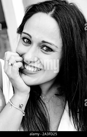 Ritratto di una giovane donna, con la mano appoggiata sulla sua bocca mentre mordere i suoi chiodi sorridente Foto Stock