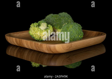 Gruppo di tre intere fresche broccoli verdi sulla piazza di legno piastra isolata sul vetro nero Foto Stock