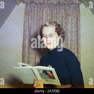 1953, storico, un elegante signora inglese che indossa un blu, rotolo di lana-collo alto e bicchieri all'interno di una sala di lettura di un libro di riferimento circa Agfacolor dal tecnico Agfa Dr. Heninz Berger. Agfacolor era il nome di una serie di film a colori prodotti realizzati da Agfa della Germania e il libro è una traduzione in inglese. Fondata a Berlino nel 1860, Agfa è entrato nel campo di photograhy nel 1898. Foto Stock