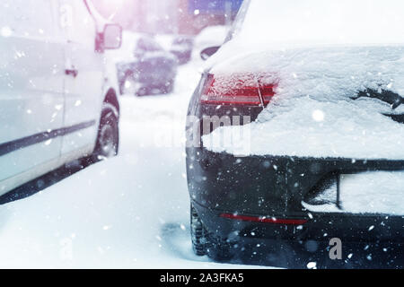 Macchina parcheggiata su una strada di città ricoperta di neve spesso strato durante la tempesta di neve la bufera di neve in inverno. Coda del veicolo a freddo inverno mattina nevicata. La sicurezza Foto Stock