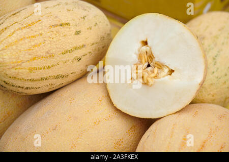 Il melone maturo tagliato a metà per la posa su un grappolo di meloni gialli. Melone con semi. Degustazione al mercato. Foto Stock