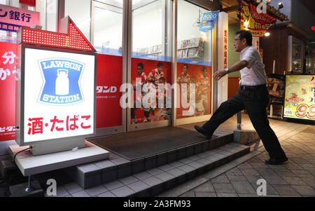 Un uomo entra in un Lawson minimarket con il Giappone Rugby World Cup promozioni sulla porta in Oita. Foto Stock