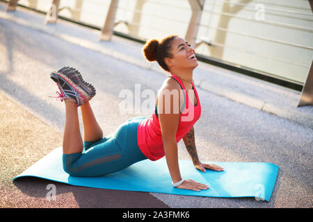 Donna sorridente praticando la sua flessibilità pur facendo yoga Foto Stock