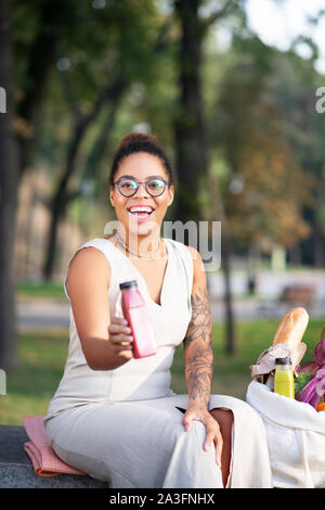 Donna con braccio tatuato tenendo la bottiglia con i frullati Foto Stock