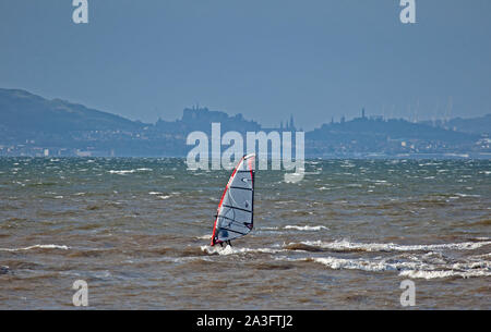 Longniddry, East Lothian, Scozia, Regno Unito. 8 ottobre 2019. Un solitario windsurf sul Firth of Forth sfidando le acque instabile con sole e vento a 45 km/h e il potenziale delle raffiche di 68 km/h. Mostra la città di Edimburgo in background con castello e Calton Hill. Foto Stock