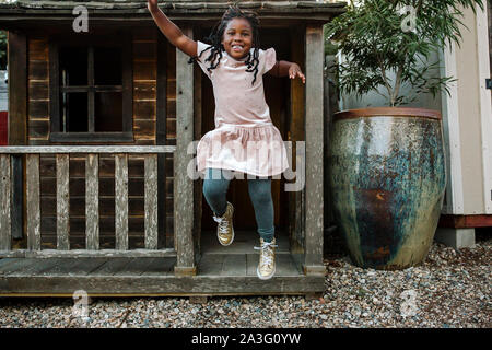 Ridendo giovane ragazza nera con lunghe trecce salto dal portico di cabina