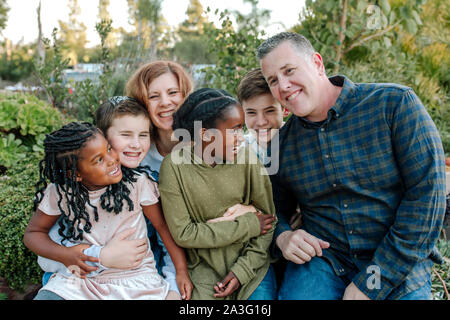 Gioiosa famiglia multirazziale ridendo e abbracciando all'aperto Foto Stock