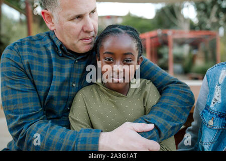 Mid-40's papà abbracciando bella sorridente giovane figlia nera all'aperto Foto Stock