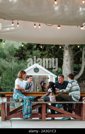 Famiglia amorevole al tavolo da picnic sotto ombrellone con multirazziale kids Foto Stock