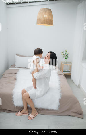 La famiglia felice. Il bambino e la madre figlia gioca, avvolgente, kissing a casa sul letto Foto Stock