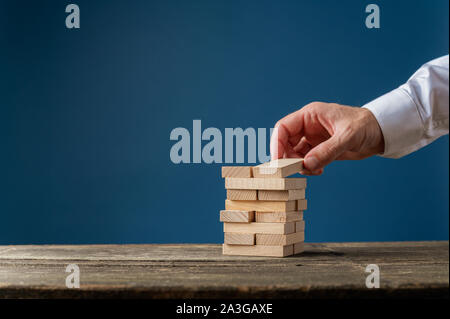 La mano di un uomo d affari con la realizzazione di una pila di picchetti di legno in una immagine concettuale. Su sfondo blu scuro con copia spazio. Foto Stock