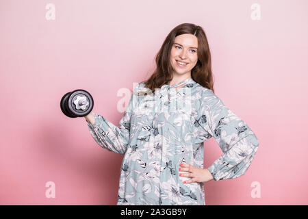 Felice giovane donna incinta indossa vestito blu fare esercizio di sollevamento pesi. Studio shot su sfondo rosa. Fitness e uno stile di vita sano durante il pr Foto Stock