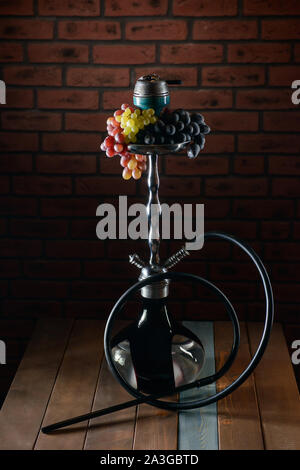 Aroma di uva hookah sul tavolo di legno sul muro di mattoni in background Foto Stock
